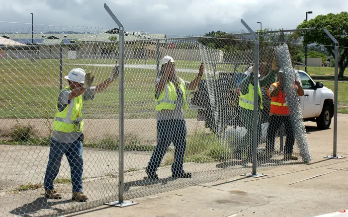 Crew stretching chain link fabric on new line posts